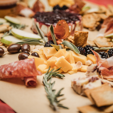 A selection of cheeses, meats, and fruits arranged on a wooden board.