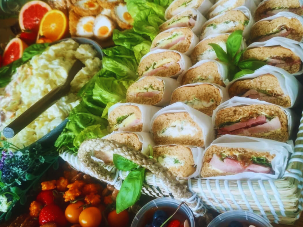 A variety of sandwiches with fresh greens, eggs, and fruits displayed on a table.