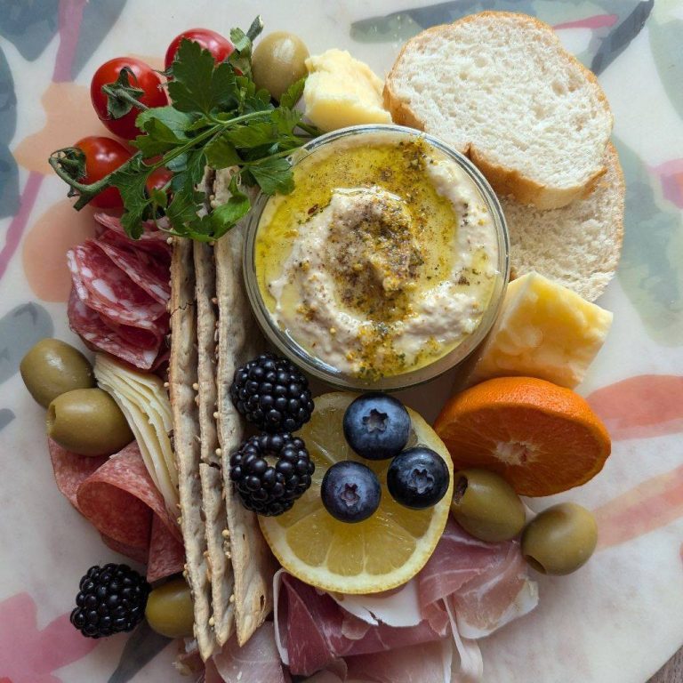 Cheese platter with red wine, grapes, and cured meats on a wooden board.