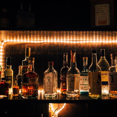 A well-stocked bar shelf with various bottles of spirits and illuminated by warm lights.